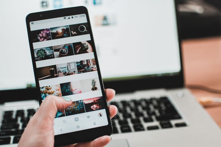Scrolling an Instagram photo feed on a smartphone in front of a laptop